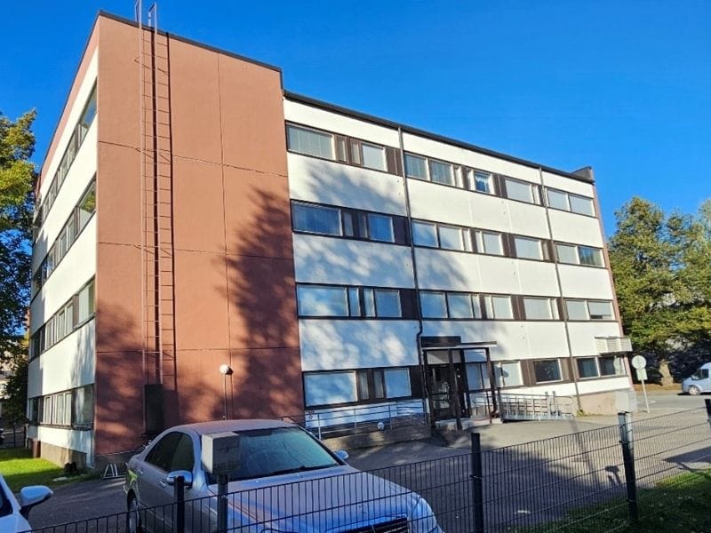 Punatiilinen kerrostalo Kuninkaankadulla, valkoiset vaakasuorat raidat julkisivussa, pysäköityjä polkupyöriä ja autoja edustalla, sekä lehtipuu etualalla