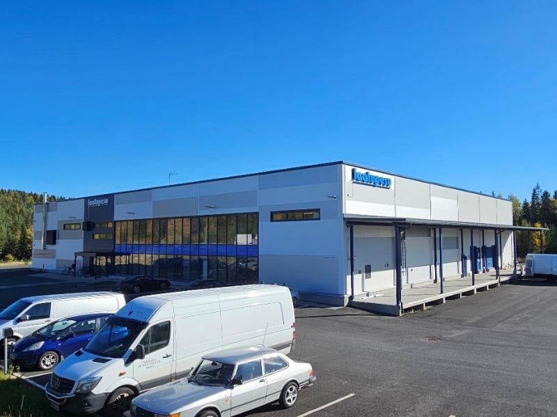 Moderni teollisuusrakennus Laatupesu-pesula, valkoinen ja sininen julkisivu, edustalla pysäköityjä pakettiautoja, sininen taivas taustalla