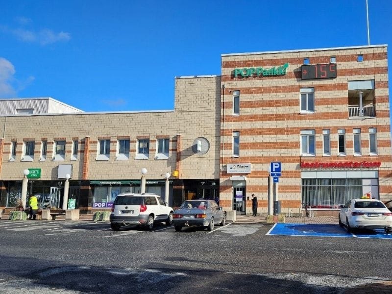 POP Pankki (800 x 600 px) Kahden kerroksen vaalea tiilirakennus, jossa on oransseja tiiliraitoja, edustalla pysäköityjä autoja ja kirkas aurinkoinen päivä