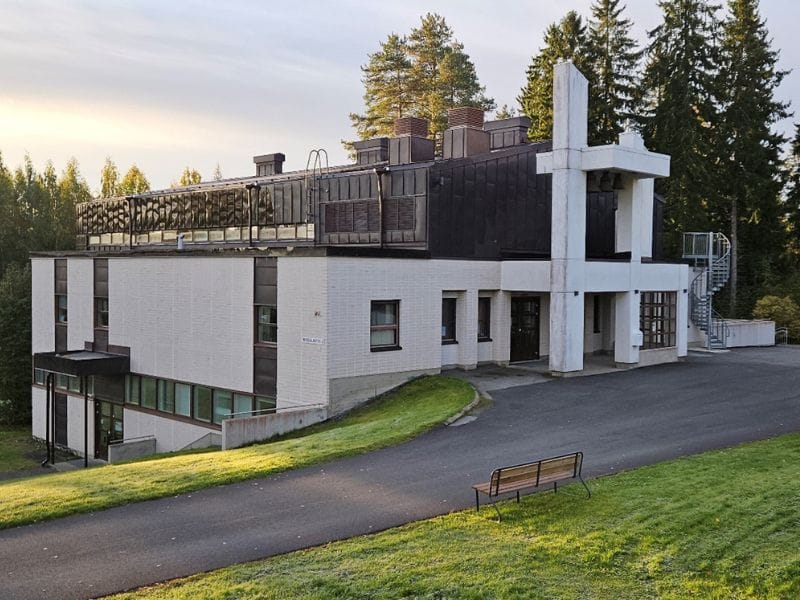 aalea, matala rakennus metsäisellä alueella, tasainen katto ja moderni arkkitehtuuri, ympärillä nurmikkoa ja kävelytie